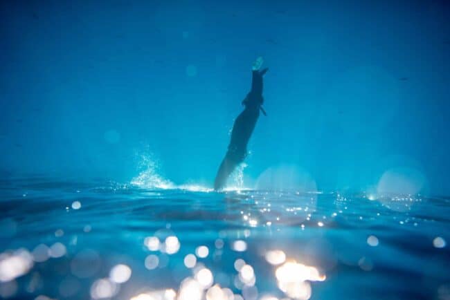 A freediver duck-diving with the surface of the water at the bottom of the image.