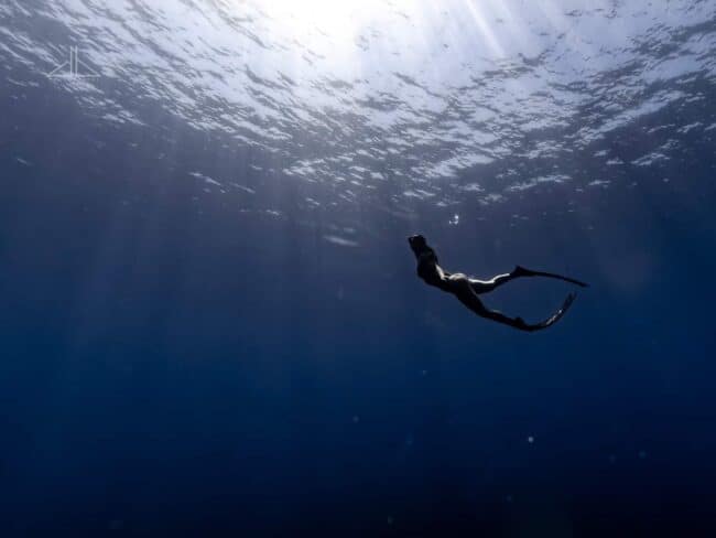 Semi-silhouette freediver swimming beneath the surface