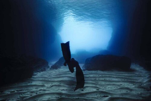 Freediver above sand exiting dark cave