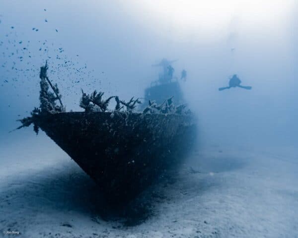 Port side bow of the P29 wreck with three SCUBA divers approaching