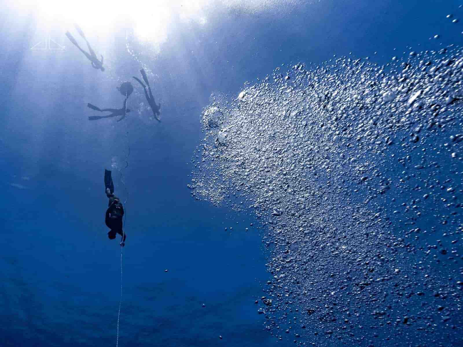 Freedivers on the surface whilst another pulls down on a line.