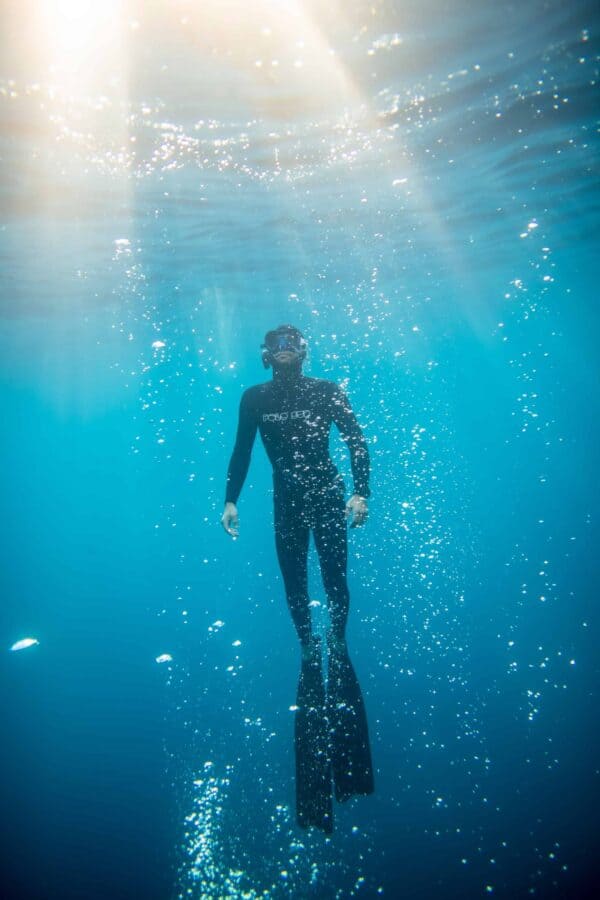 Close shot of freediver surfacing into ray of light