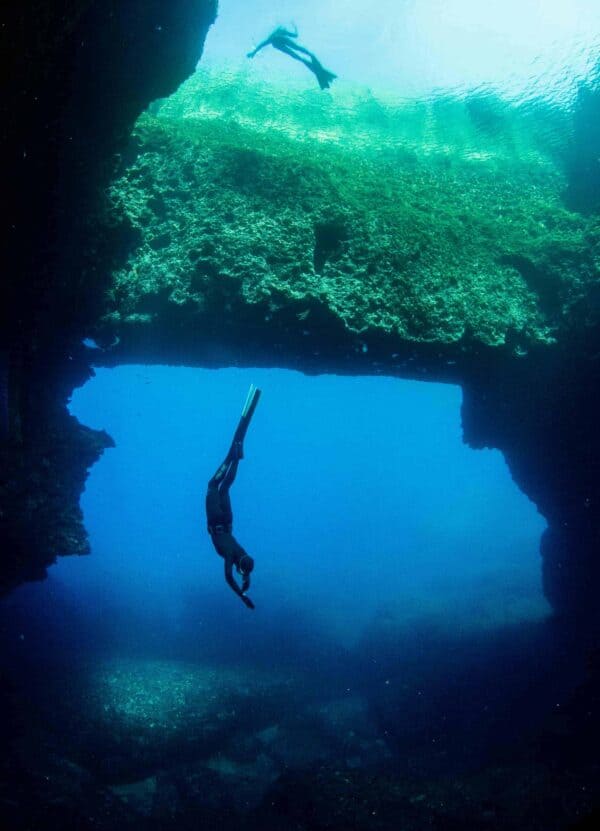 Freediver diving and stretching out with Clue Hole arch behind her