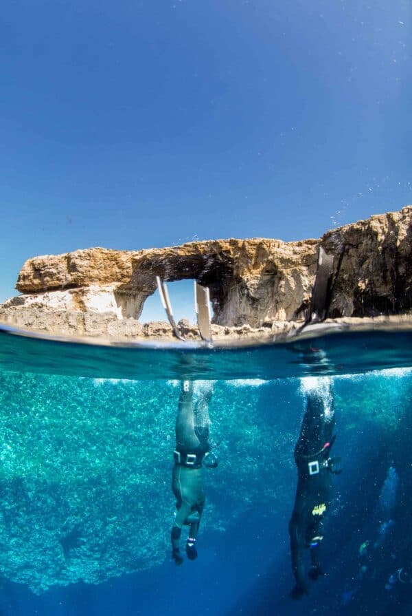 Half water half air on surface. Two freedivers duck dive into Blue hole