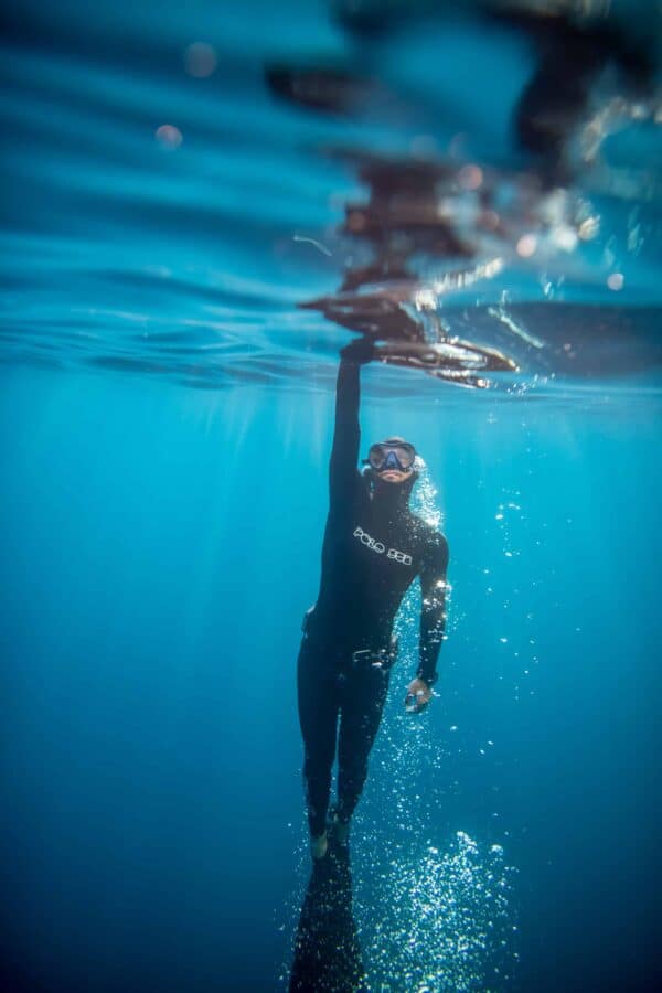 Freediver surfacing in the Maltese waters, with his arm above his head, just before surfacing.