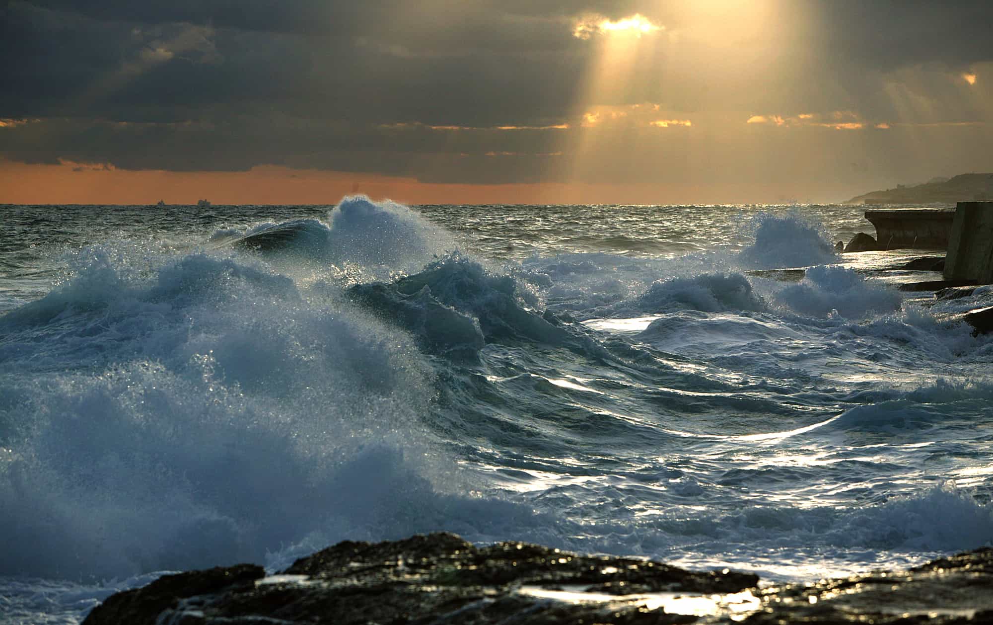 Waves crashing against the rocks with sun rays in the back ground.